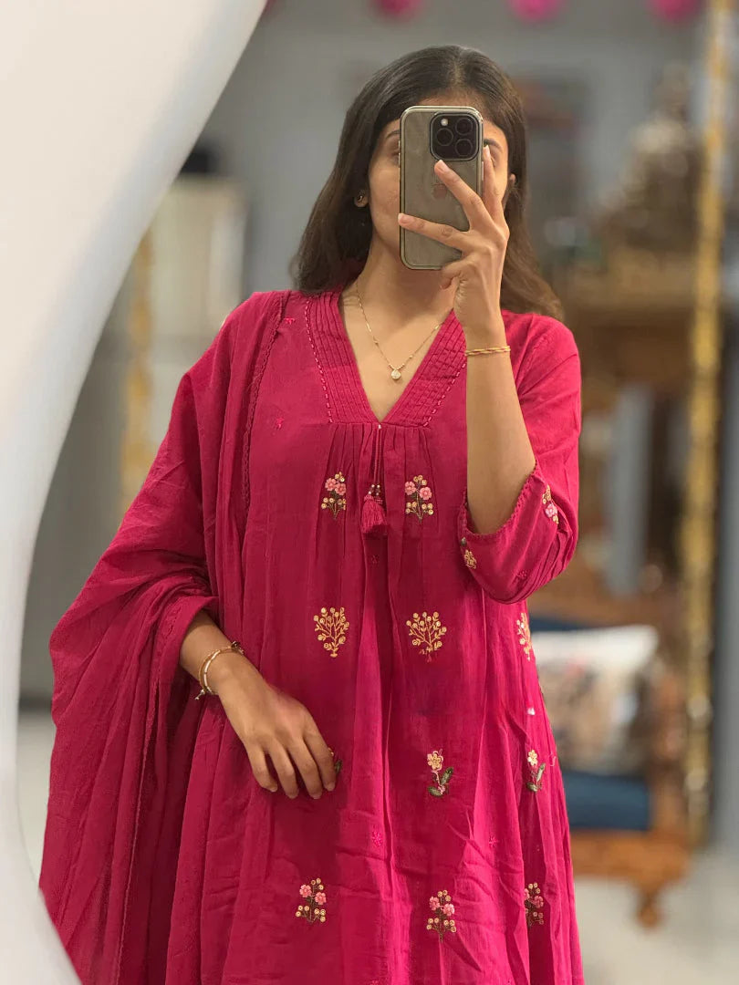Close-up mirror selfie of a woman wearing a vibrant rani pink flared kurta highlighting the floral embroidery and V-neck detailing with tassels.