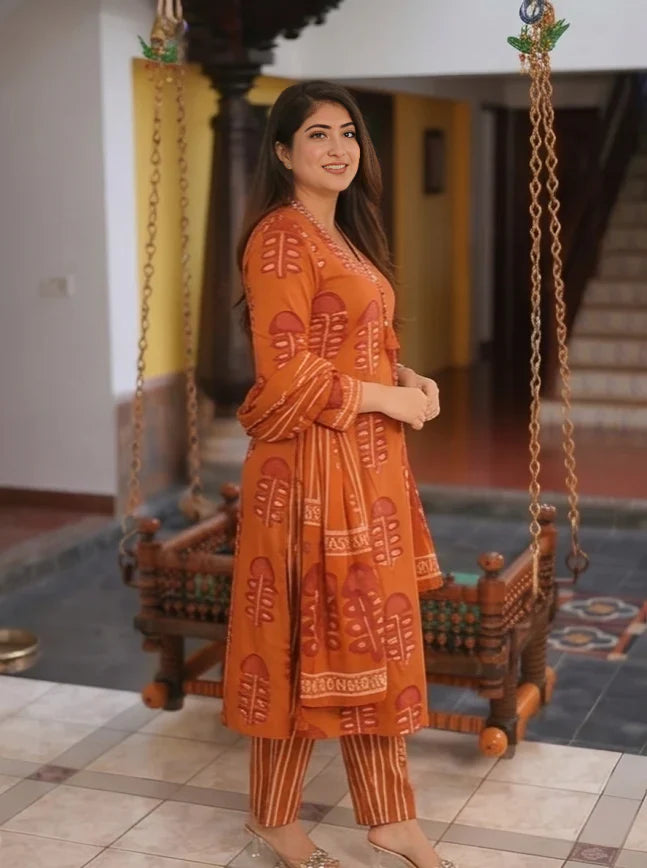 Side profile of a woman elegantly posing in a rust orange printed pure cotton suit set with a matching dupatta.