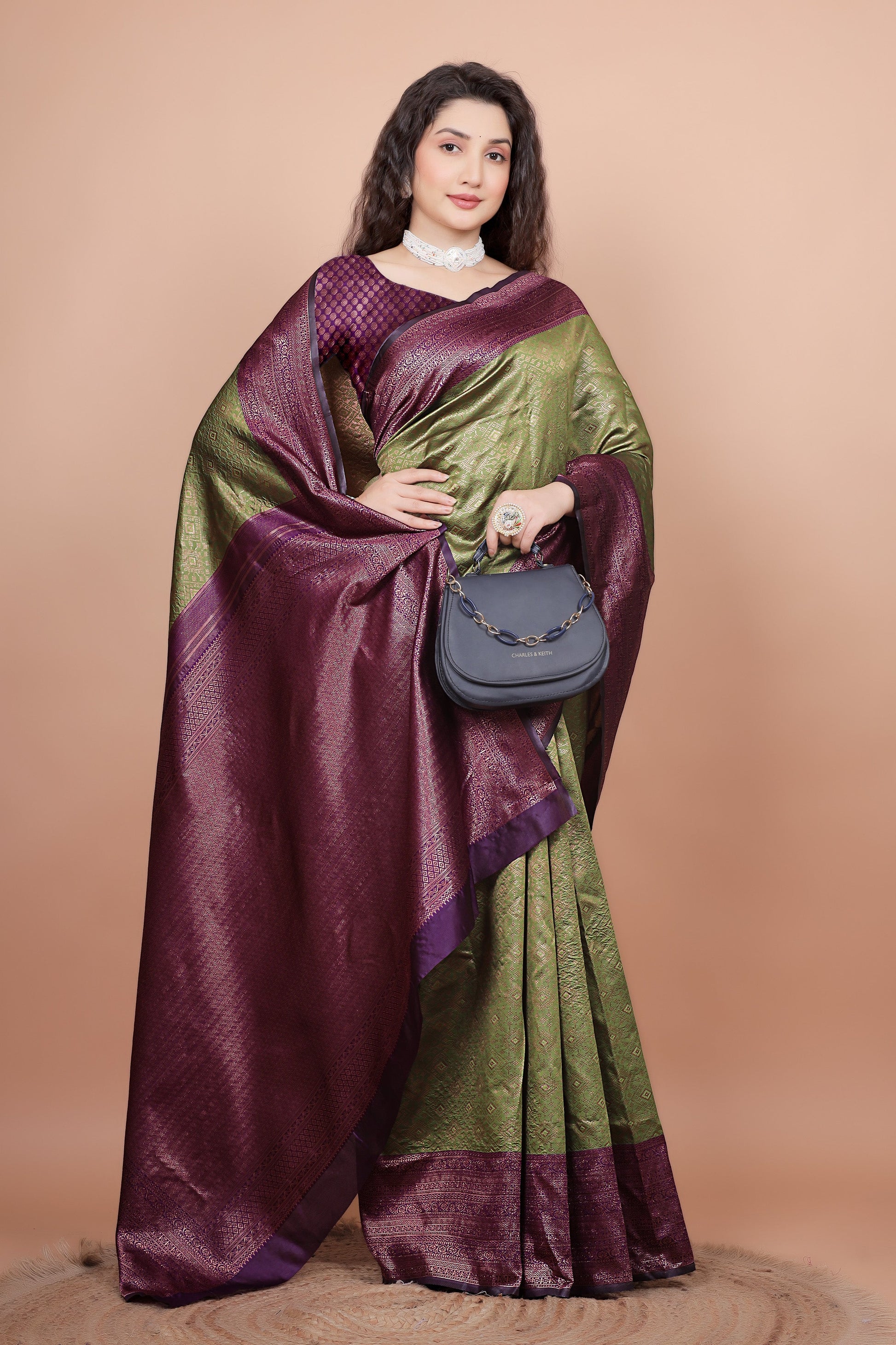 Model elegantly draped in a mehndi and cherry silk saree, holding a stylish bag