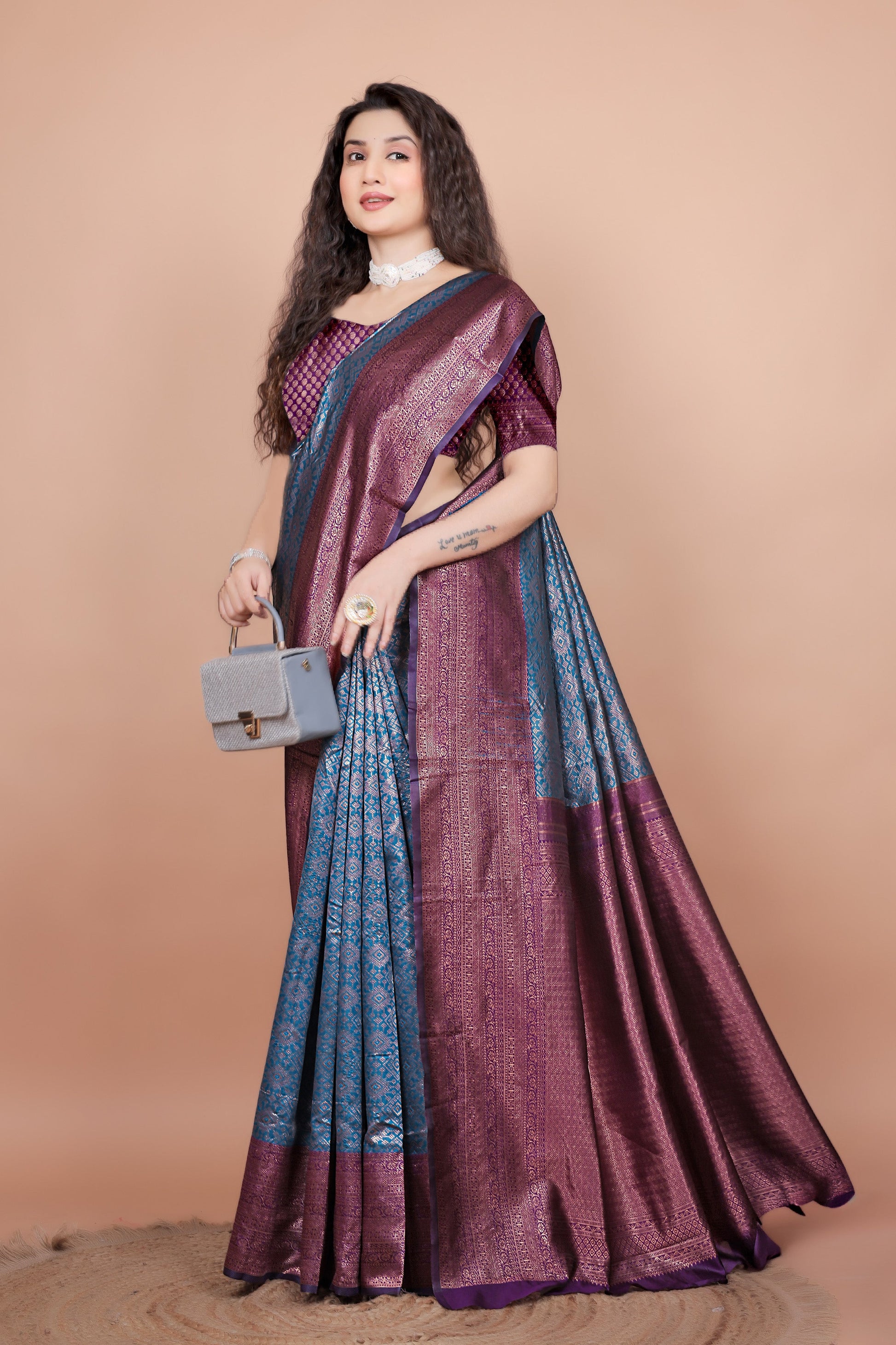 Model elegantly draped in a peacock blue and wine silk saree, posing with a stylish handbag