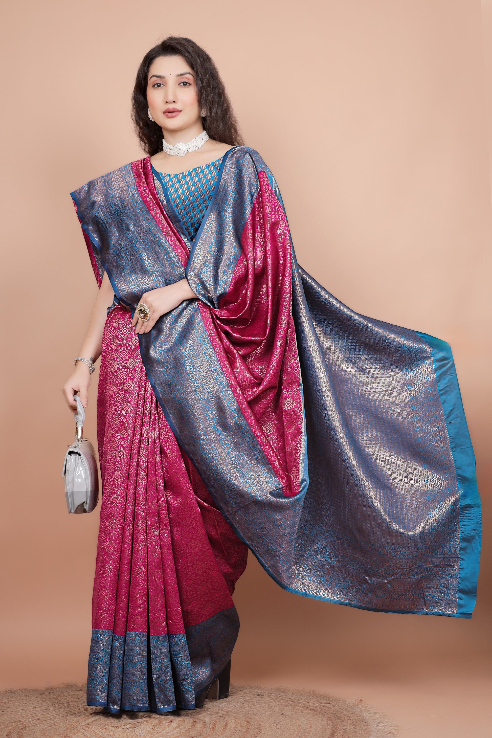 Posed shot of a woman in a rani pink traditional silk saree holding a stylish bag