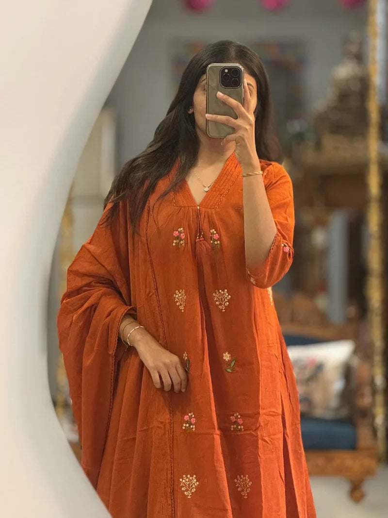 Close-up mirror selfie of a woman wearing a warm rust orange flared kurta highlighting the floral embroidery and V-neck detailing with tassels.